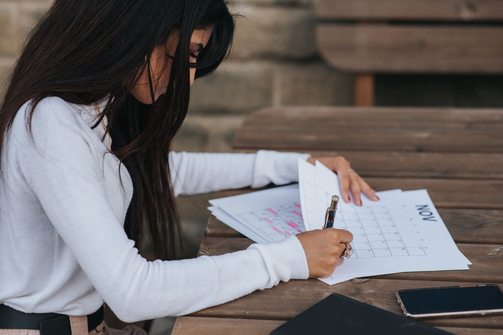 Young woman planning her month in a paper calendar at an outdoor table