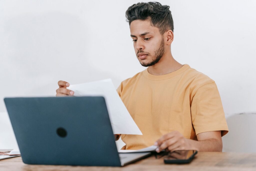 Young adult reviewing a bill beside a laptop while learning financial literacy basics