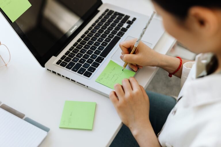 Young adult writing notes beside a laptop while learning practical life skills for adulthood