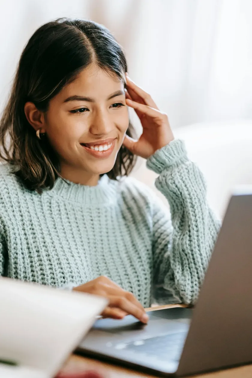 Smiling young woman in a sage sweater calmly sorting her money, career and life admin on a laptop at home