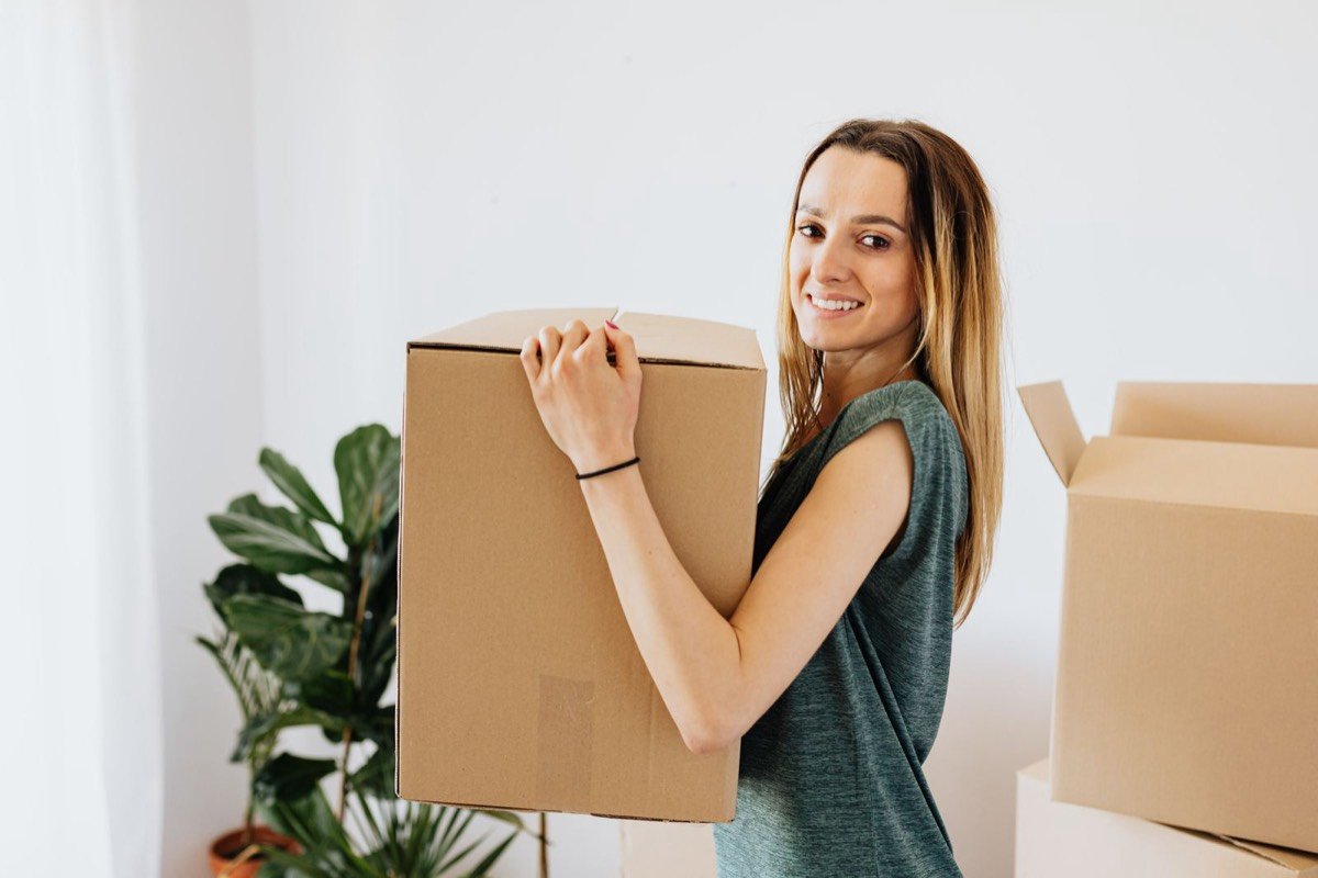 A young woman carrying a moving box in a bright apartment on moving day