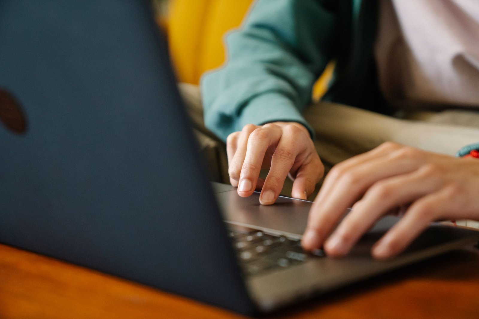 Person typing on a laptop at a warm wooden desk, the focused computer work AI training jobs involve