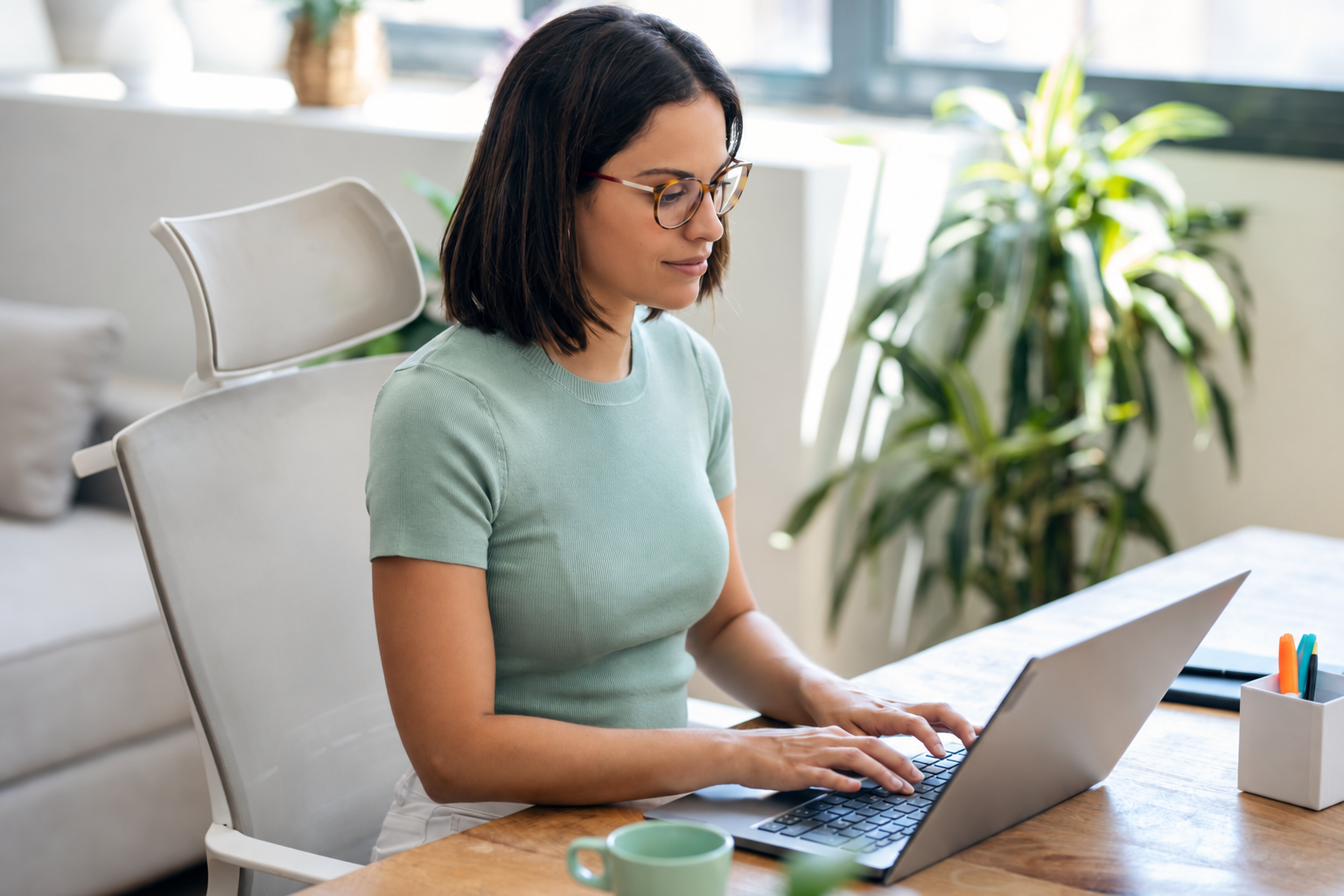 Young professional woman in a mint green top working on a laptop at a desk