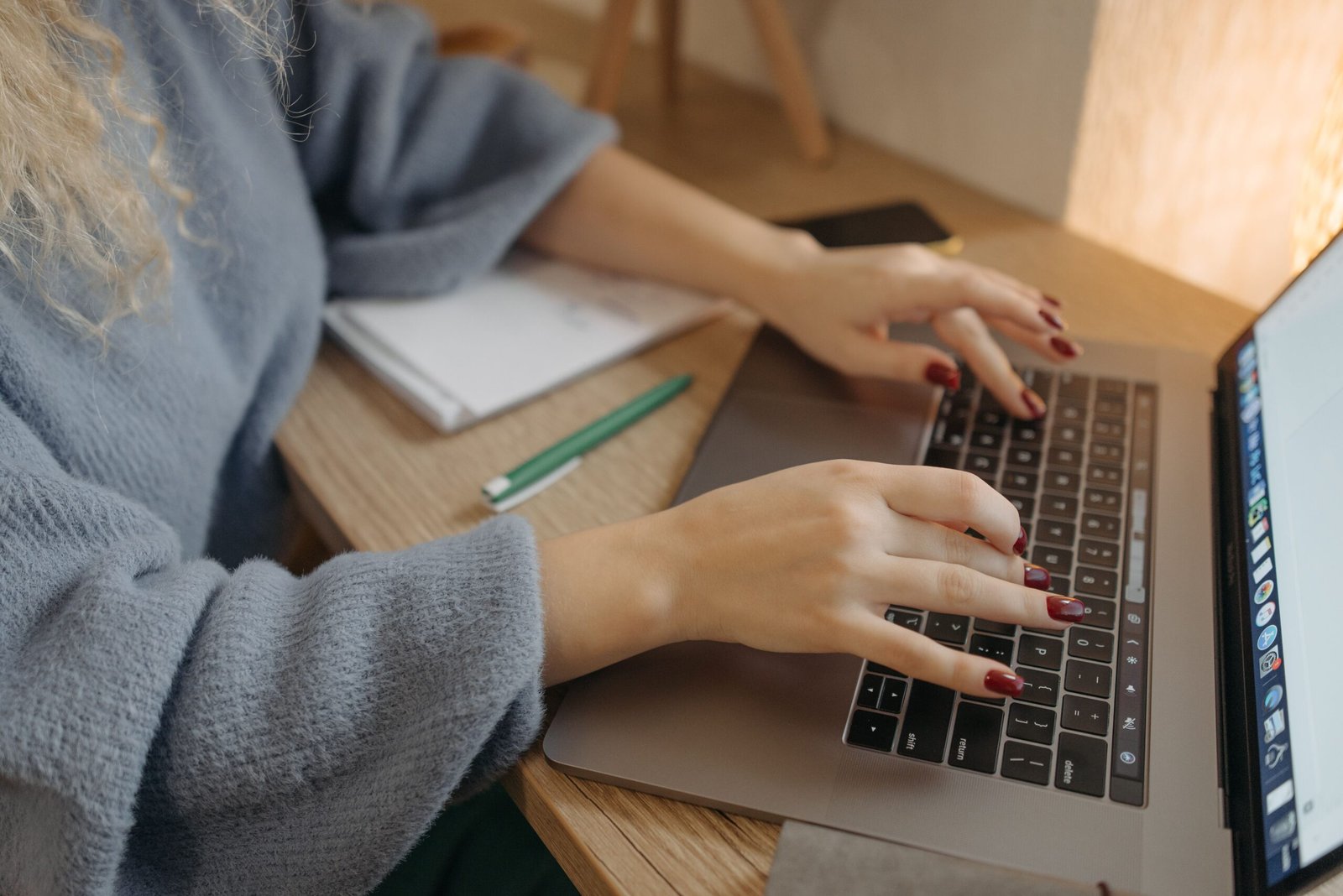 Close-up of hands typing on a laptop at a wooden desk with a notebook and pen nearby, drafting a part-time resume