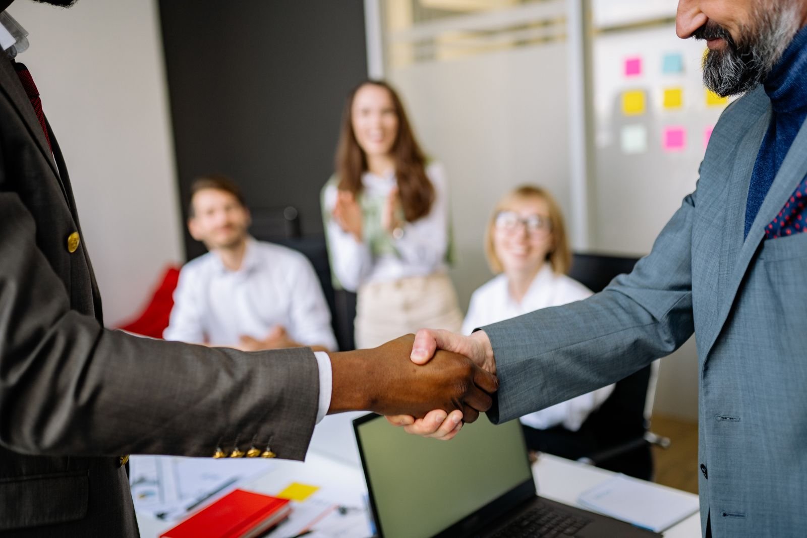 Two colleagues shaking hands over a boardroom table after reaching an agreement